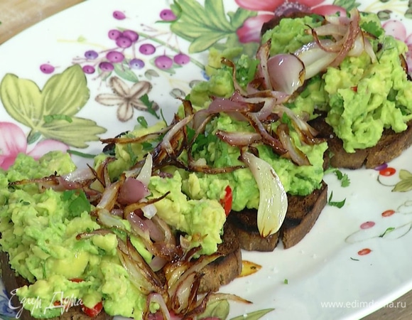 Поджаренные тосты выложить на большую тарелку, намазать гуакамоле, посолить, посыпать оставшейся кинзой, сверху разложить поджаренный лук.