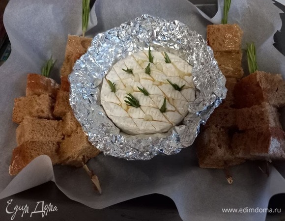 Форму для запекания застилаем пекарской бумагой, выкладываем сыр в фольге и шпажки с хлебом. Хлеб поливаем еще одной чайной ложкой оливкового масла.