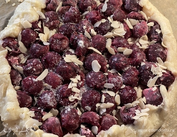 Вишню очистить от косточек, дать стечь лишней жидкости. При помощи сита посыпать поверхность теста крахмалом. Выложить вишню, не доходя до края 2 см, посыпать сахаром и миндальными лепестками. Загнуть края по всему периметру и прижать, формируя пирог. Края слегка смазать водой и посыпать сахаром.