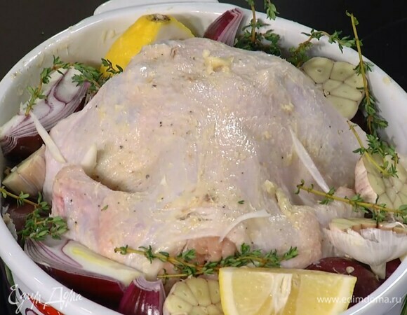 Грудку курицы, приподняв кожу, смазать пряным маслом, затем промазать всю тушку внутри и снаружи и поместить в жаропрочную форму, рядом выложить нарезанный лук, чеснок, лимон и веточки тимьяна (немного оставить для украшения).