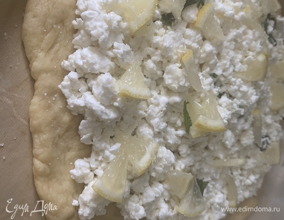 Тесто разделить на 2 части. Большую часть раскатываем на основу. Можно сделать все руками, как бы растягивая. Сверху выкладываем творожную начинку, дольки лимона, которые слегка посыпаем сахаром.