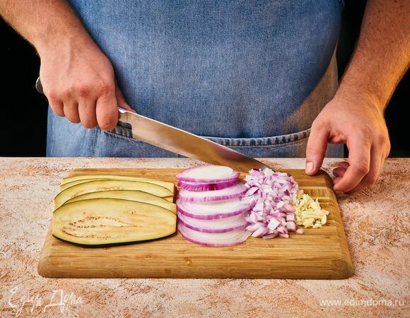 Баклажаны нарежьте вдоль тонкими слайсами. Часть лука нарежьте мелким кубиком, вторую часть — кольцами. Чеснок мелко порубите.