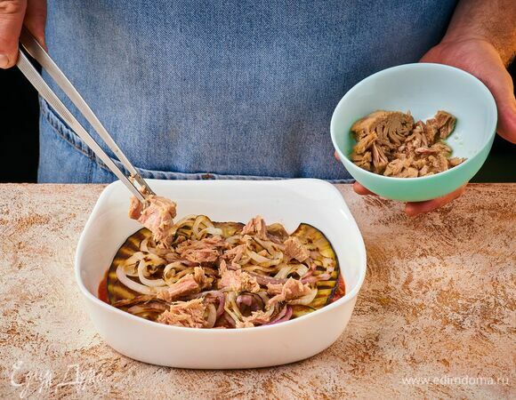 Выложите в форму часть готового соуса, затем — слой баклажана и лука. Далее — слой консервированного тунца.