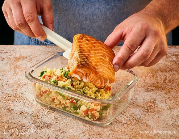 Выложите в контейнер кускус с овощами, а сверху — жареную рыбу.
