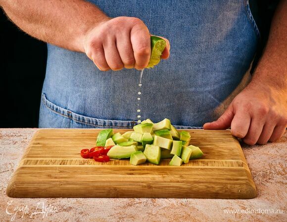 Приготовьте соус гуакамоле. Крупно нарежьте мякоть авокадо, полейте соком половины лайма. Перец мелко порубите.