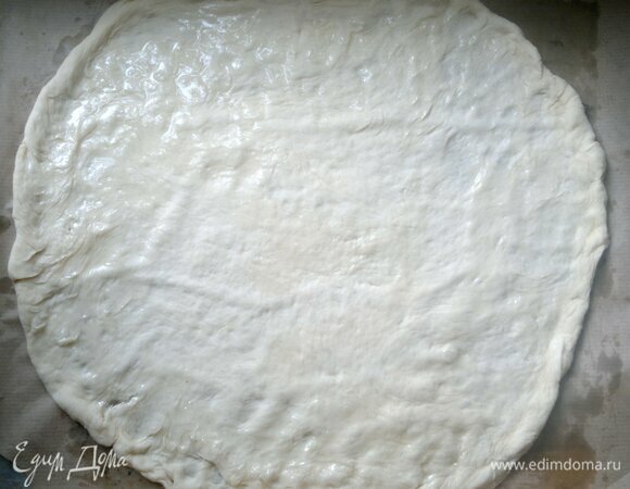 Переложить тесто на противень с пергаментом. Масло с чесноком выложить на сито и отцедить от чеснока. Смазать ароматным маслом основу для пиццы.