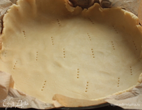 Охлажденное тесто быстро раскатайте между двух пергаментов, выложите в форму и наколите вилкой.