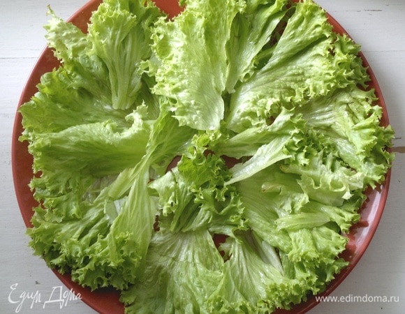 Листья салата порвать руками на большие кусочки и выложить их на плоское блюдо.