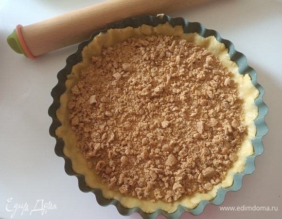 Форму смазать маслом и посыпать мукой. Достать тесто из холодильника, разделить его на 2 неравные части. Большую часть раскатать и уложить в форму, сделав невысокий бортик. На дно песочной основы выложить печенье, предварительно измельчив его руками.