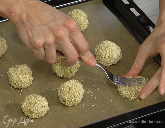 Сформировать из теста небольшие шарики, обвалять в кунжуте, выложить на застеленный бумагой для выпечки противень и прижать каждый шарик вилкой так, чтобы получились лепешки.