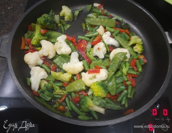 Теперь нам нужно подготовить овощи. Овощную смесь высыпаем в сковороду, включаем плиту на средний огонь и заливаем 50 мл горячей воды, помешиваем примерно раз в минуту. Так овощи быстрее разморозятся.