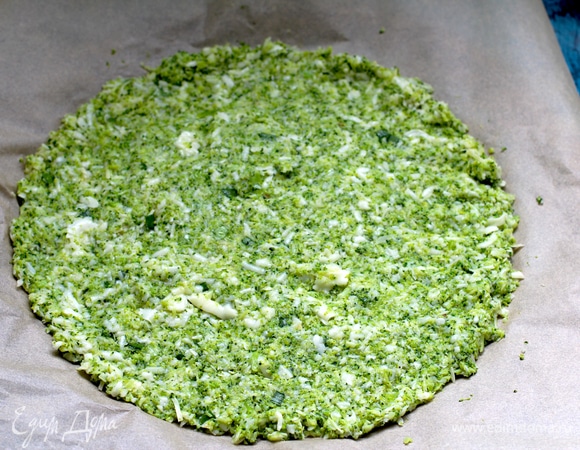 Остужаем полностью, перекладываем на гладкое полотенце или марлю и очень тщательно отжимаем, стараясь удалить как можно больше жидкости — это важно! В отжатую досуха брокколи добавляем все остальные ингредиенты для основы, вымешиваем до однородности. Перекладываем на бумагу для выпечки и распределяем толщиной около 1 см (диаметр около 35 см).