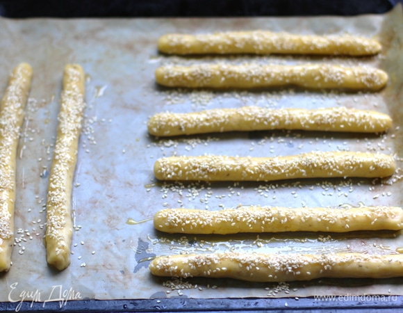 Положите палочки на застеленный пергаментом противень, смажьте взбитым желтком, посыпьте кунжутом. Поставьте противень в предварительно разогретую до 180°C духовку на 15 мин.