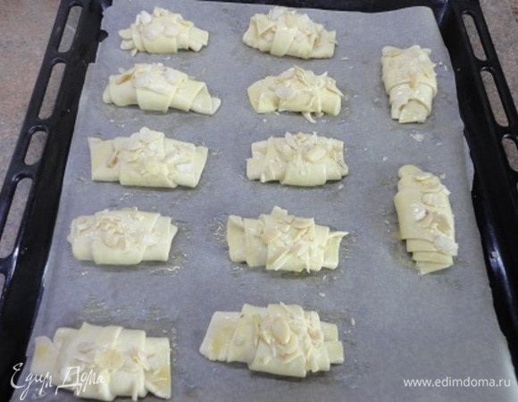 Если вы используете дрожжевое тесто, дайте заготовкам расстояться 20–25 минут. Перед выпеканием смазываем их яйцом и посыпаем миндальными лепестками. Выпекаем 20 минут при 200°C.