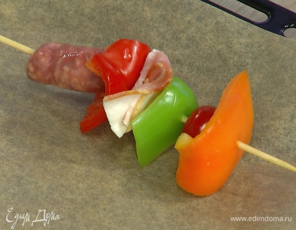 На каждую деревянную шпажку нанизать колбаску, кусочек перца, сложенный в несколько раз кусочек бекона, кусочек перца, помидор черри и снова кусочек перца.