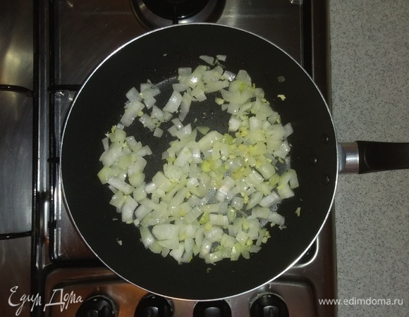 Сковородку смазать оливковым маслом и обжарить на ней нарезанный репчатый лук до мягкости вместе с измельченными зубчиками чеснока (на среднем огне маленькой конфорки плиты).