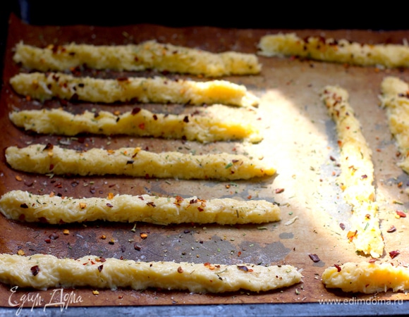 Из теста сформировать длинные тонкие жгутики (это сложно, тесто не держит форму, не тянется, все делала непосредственно на тефлоновом коврике мокрыми руками), слегка посыпать крупной солью, сухими травами, хлопьями чили (советую их добавить, придают пикантности блюду и являются хорошим дополнением сырному вкусу).