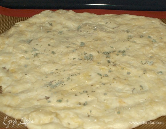 Тесто накрыть полотенцем и отставить на 20–30 минут. Спустя указанное время тесто распределить на противне. Тесто очень легкое в работе, легко распределяется руками. Можно воспользоваться скалкой. Смазать лепешку растительным маслом (достаточно одной чайной ложки), посыпать орегано.