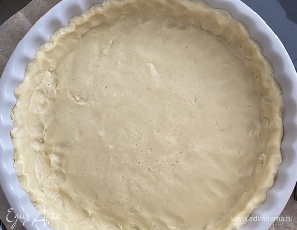 Разъемную форму диаметром 28 см смазать тонким слоем сливочного масла. Я взяла обычную керамическую форму, но это было ошибкой — пирог очень сложно потом вытаскивался. Тесто раскатать в круг между двумя слоями пергамента и выложить в форму тонким слоем (~ 0,5 см). Сделать бортики высотой 2–2,5 см. Опять убрать форму в холод на 15 минут.