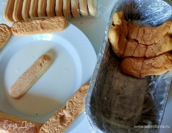 Прямоугольную форму застелить пищевой пленкой в два слоя. Печенье слегка смочить в молоке и выложить на сухую поверхность буквально на 5–10 секунд. Затем уложить печенье в форму вплотную друг к другу.