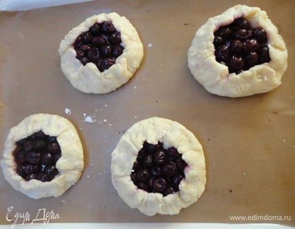 Разделить тесто на 8 частей, каждую скатать в шар. Руками сформировать из каждого шара лепешечку с утолщениями по краю в качестве бортиков. Выложить на противень. На каждую ватрушку распределить по половике чайной ложки крахмала, выложить вишню, смазать края молоком и посыпать штрейзелем. По желанию можно до штрейзеля посыпать вишню коричневым сахаром. Выпекать 16–20 минут.