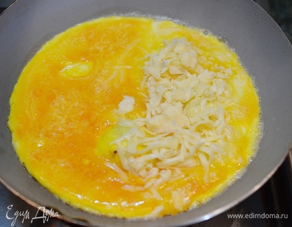 Когда омлет схватится по краям, половину омлета посыпьте сыром.