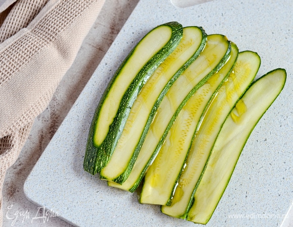 Некрупный цукини нарезаем вдоль. Сбрызгиваем оливковым маслом.