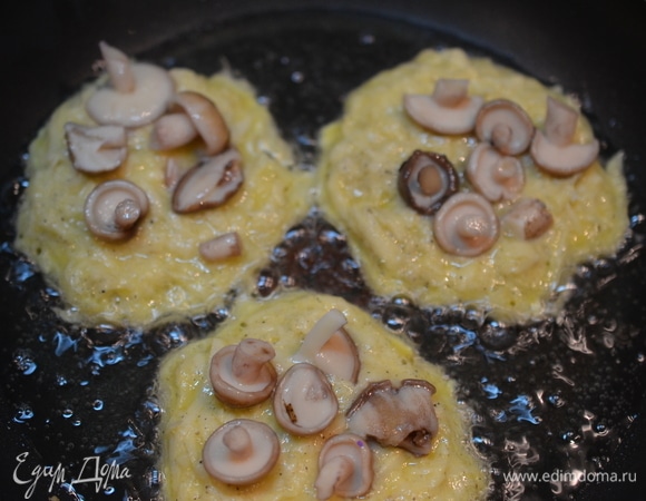 Пока драники жарятся с одной стороны, положите на непрожаренную сторону немного грибов.