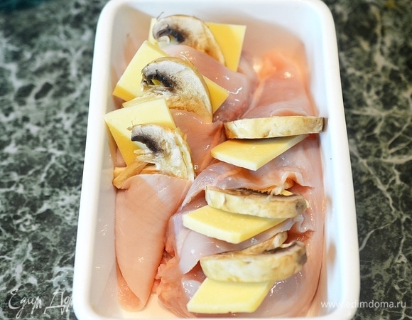 В каждый надрез вставьте по ломтику шампиньона и сыра. Выложите грудки в жаропрочную форму.
