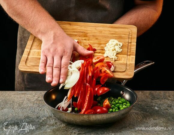 На сковороде в оливковом масле обжарьте лук и чеснок. Добавьте болгарский перец, помидоры черри и горошек. Обжаривайте, помешивая, 5 минут.