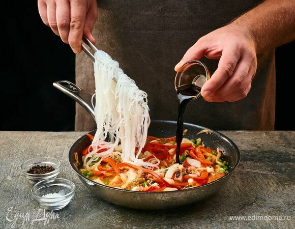 К овощам добавьте фунчозу и соевый соус. Чуть посолите, поперчите и перемешайте.