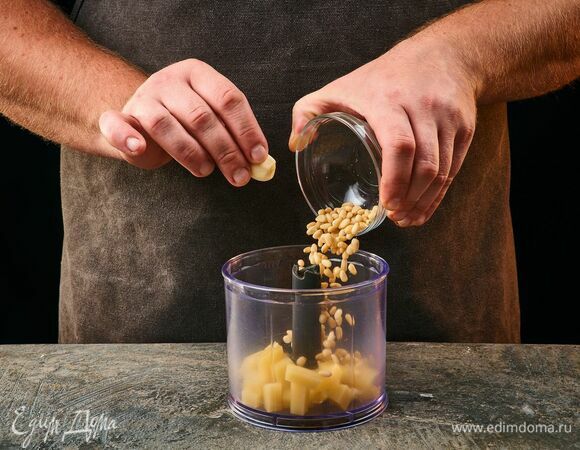 Чтобы приготовить песто, выложите в чашу блендера пармезан, зубчик чеснока и кедровые орехи.