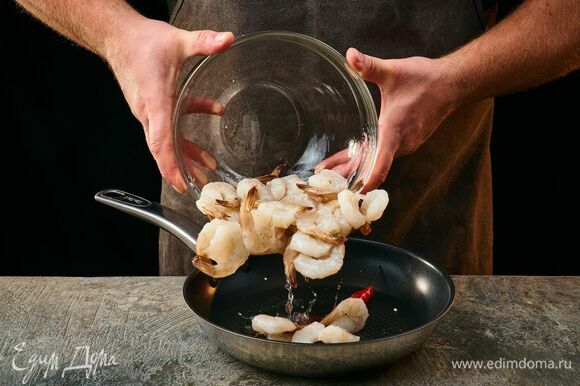 На сковороду с разогретым оливковым маслом выложите королевские креветки и обжаривайте 2 минуты. Добавьте перец чили. Жарьте все вместе еще около 5 минут.