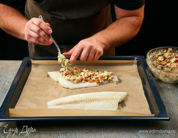 Рыбу обсушите, выложите на противень, застеленный пергаментной бумагой. Равномерно распределите грибную смесь по рыбному филе. Запекайте палтуса в предварительно разогретой духовке при 220°C около 8–10 минут.