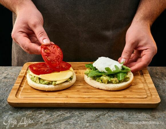 На одну половину булочки выложите половину пюре из авокадо, руколу и яйцо пашот. На другую половину булочки выложите оставшееся пюре из авокадо, тонко нарезанное манго, ломтики помидора.