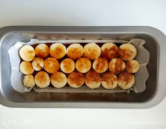 Форму для кекса застелить пергаментной бумагой. Дно полить карамелью. Затем выложить бананы, предварительно нарезав их кружочками толщиной 1 см. Сверху полить карамелью.