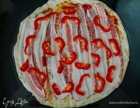 Затем на пиццу выложить полоски бекона и нарезанный красный болгарский перец. Посолить сверху.