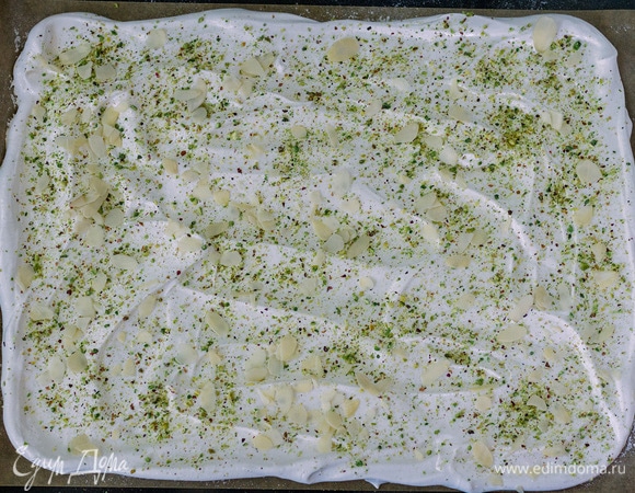 Противень застелить бумагой для выпечки и слегка посыпать сахарной пудрой, выложить готовую меренгу, сформировать прямоугольник и посыпать сверху крошкой из фисташек и миндальными лепестками. Выпекать при 110°C 30–40 минут.