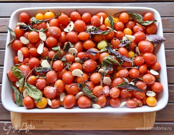 Помидорки мою, сушу, выложив на бумажное полотенце. В подготовленную огнеупорную форму выкладываю томаты. Добавляю нарезанный пластинками чеснок, листья базилика, туда же отправляю стебли. Солю и посыпаю сахаром. Вливаю оливковое масло. Перемешиваю аккуратно, стараясь не повредить целостность.