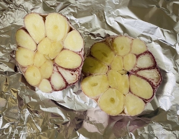 Головку чеснока разрезать поперек на 2 равные части. Плотно обернуть фольгой и запекать в духовке при 180°C 15–20 минут.