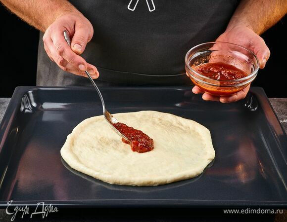Готовое тесто раскатайте в круг, толщиной до 0,5 см. Смажьте тесто томатным соусом.