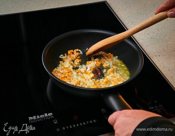 На индукционной панели конфорок Miele разогрейте сковороду со сливочным маслом. Обжарьте лук, чеснок, морковь, а затем переложите из сковороды в тарелку.