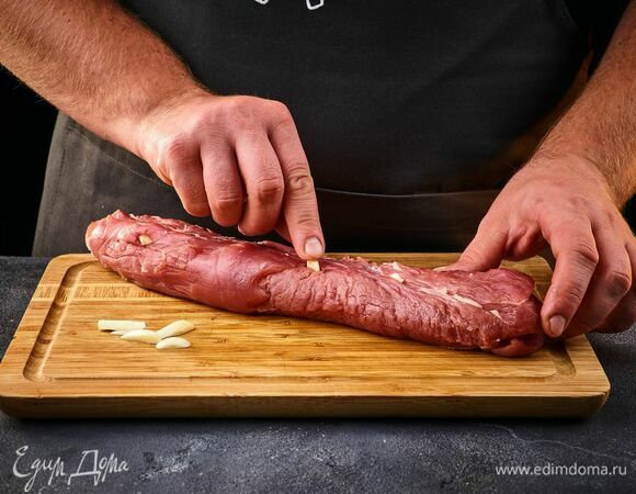 Чеснок почистите и нарежьте крупными кусками. Сделайте на свинине надрезы и поместите туда кусочки чеснока.