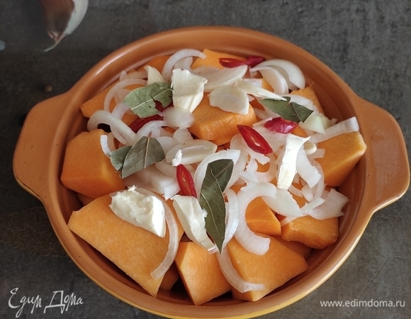 Сверху выложить нарезанный полукольцами лук, зубчики чеснока, лавровый лист, немного перчика чили. Кусочек сливочного масла (30 г) разрезать на несколько частей и тоже положить сверху тыквы. Долить 100 мл воды, чтобы тыква не подгорела, накрыть фольгой и поставить запекаться в духовку, разогретую до 180°C, на 40 минут.