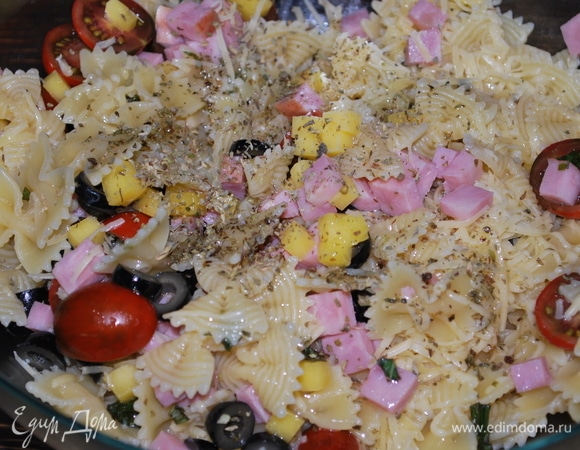 В большой миске соедините ветчину, сыр, оливки. Готовую пасту откиньте на дуршлаг, чтобы стекла вода, и добавьте ее в миску. Свежий базилик мелко нарежьте, добавьте по вкусу свежемолотый черный перец, орегано и оливковое масло. Все перемешайте, отрегулируйте вкус с помощью трав и оливкового масла.