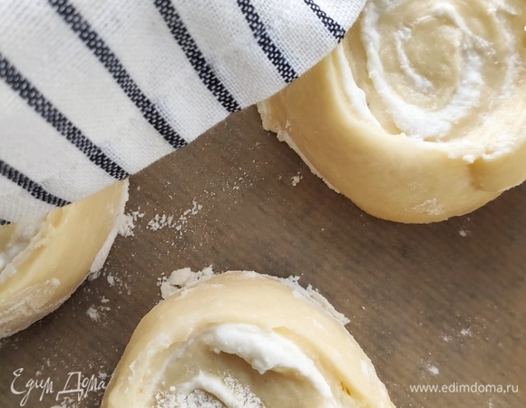 Творог взбиваем блендером с 3 ложками сахара, трем лиммоную цедру на мелкой терке и отправляем к творогу. Подошедшее тесто раскатываем в пласт шириной примерно 2–3 мм, выкладваем нашу массу и сворачиваем в рулет. Нарезаем на небольшие кусочки, выкладываем на противень, на котором уже лежит пергамент, смазанный сливочным маслом. Накрываем полотенцем и даем еще постоять 25 мин. Смазываем булочки желтком и отправляем в духовку, разогретую до 180°C, на 25–30 минут.