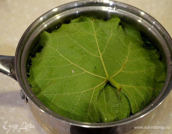 Выложите в сотейник, сверху также накройте виноградными листьями. Залейте бульоном. Можно и водой, но с бульоном гораздо вкуснее. Доведите до кипения и готовьте на небольшом огне, накрыв крышкой, около 45 минут.