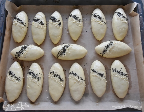 Готовые пирожки укладываю на противень, выстеленный пергаментной бумагой, и оставляю на 20 минут для расстойки. Верх пирожков смазываю яичным желтком, смешанным с молоком, и посыпаю кунжутом. Выпекаю пироги в духовке, разогретой до 180°C, 30 минут.