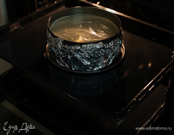 В глубокий противень влить горячую воду и поставить на нижний ярус духовки. Чизкейк выпекать на противне посередине при 115°C в течение 90–120 минут. Готовность определяется слегка дрожащей серединой.