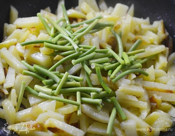 Когда картофель обжарится до полуготовности, добавьте чесночные стрелки. Предварительно их, конечно, вымойте, обсушите и нарежьте. У меня длинные стрелки, но можно мелко их порубить.